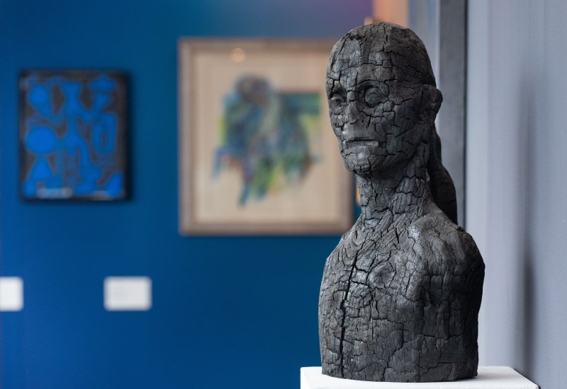 Statua di una donna frammentata di colore grigio, sullo sfondo 2 quadri