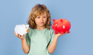 Mädchen mit zwei Sparschweinen in Form von Schweinen, eines rot und eines weiß, in den Händen