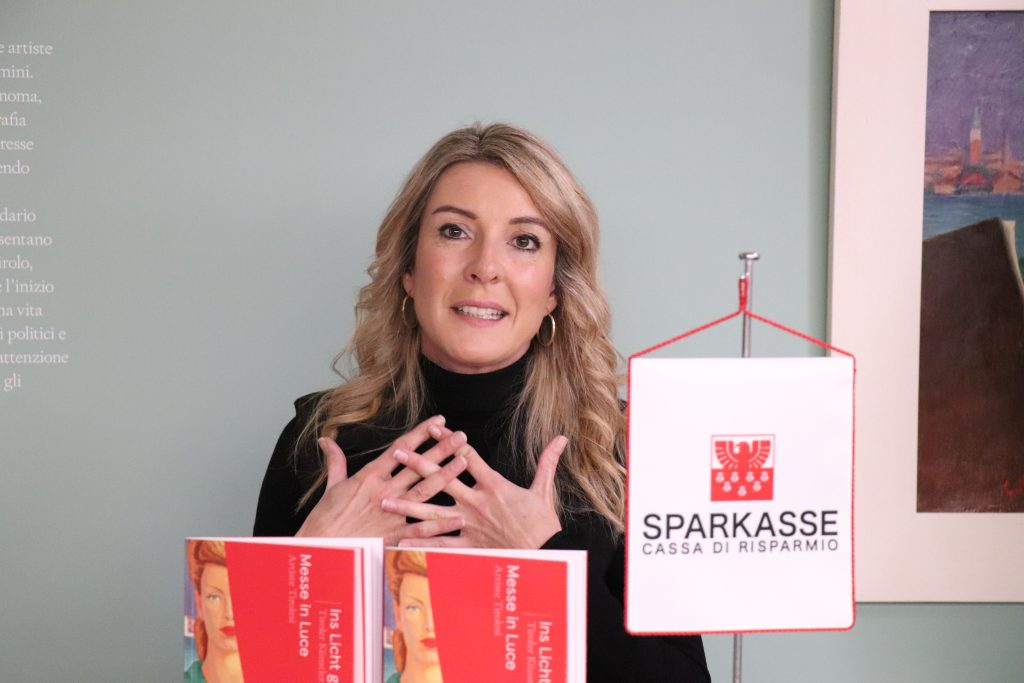Lisa Trockner con davanti 2 libri rossi e uno stendardo con il logo e la scritta Sparkasse