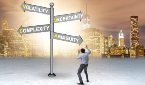 Uomo davanti ad un cartellocon la scritta Volatility, Uncertainty, Complexity, Ambiguity ed nello sfondo uno skyline
