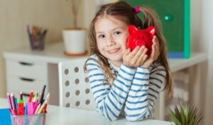 Mädchen in einem Zimmer mit einer roten Sparbüchse in Form eines Schweins in der Hand